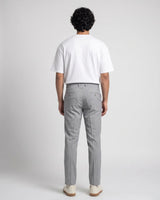 A man standing against a light gray studio background wearing a plain white short-sleeve crewneck t-shirt, light gray trousers, and off-white sneakers.