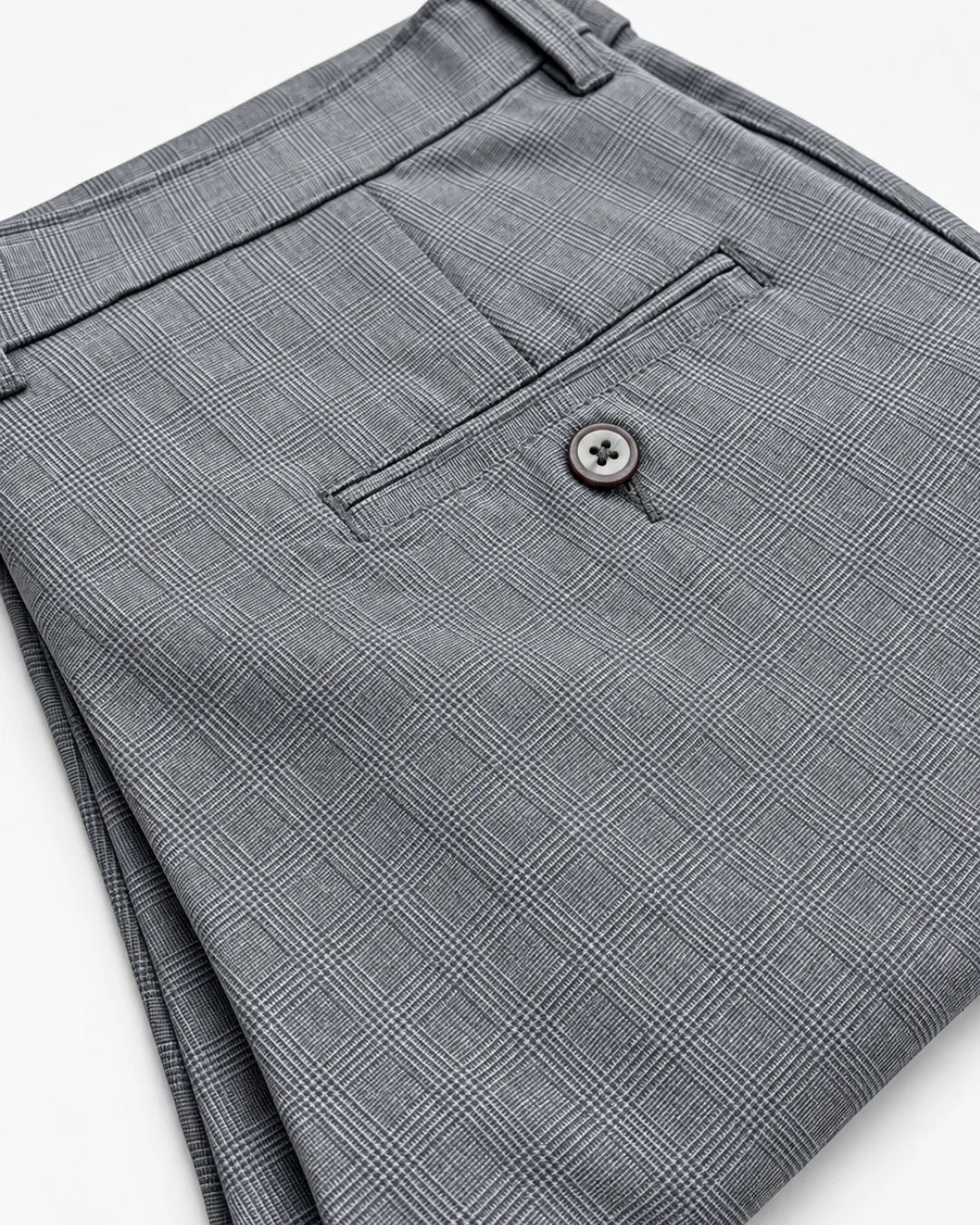 Close-up of folded gray plaid trousers showing the back pocket with a button closure and belt loop.