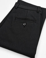 Black plaid trousers folded to show the back pocket with a button closure, on a white background.