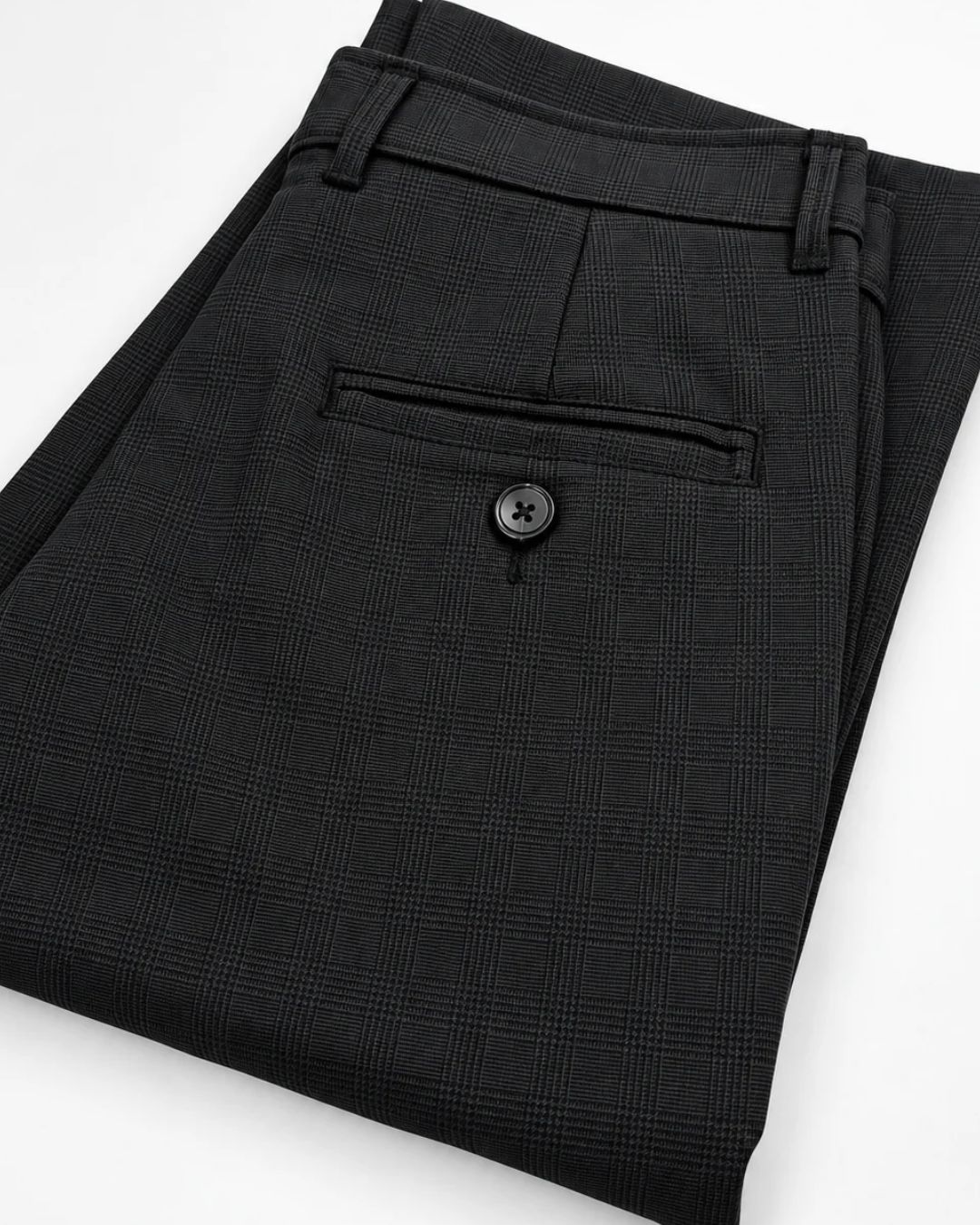 Black plaid trousers folded to show the back pocket with a button closure, on a white background.
