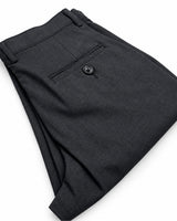 A close-up of folded dark charcoal gray dress pants showing the waistband, belt loops, a back pocket with a button, and the fabric texture on a white background.