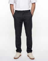 A person wearing slim-fit black trousers, paired with a white short-sleeve shirt and off-white sneakers, standing against a plain white studio background.