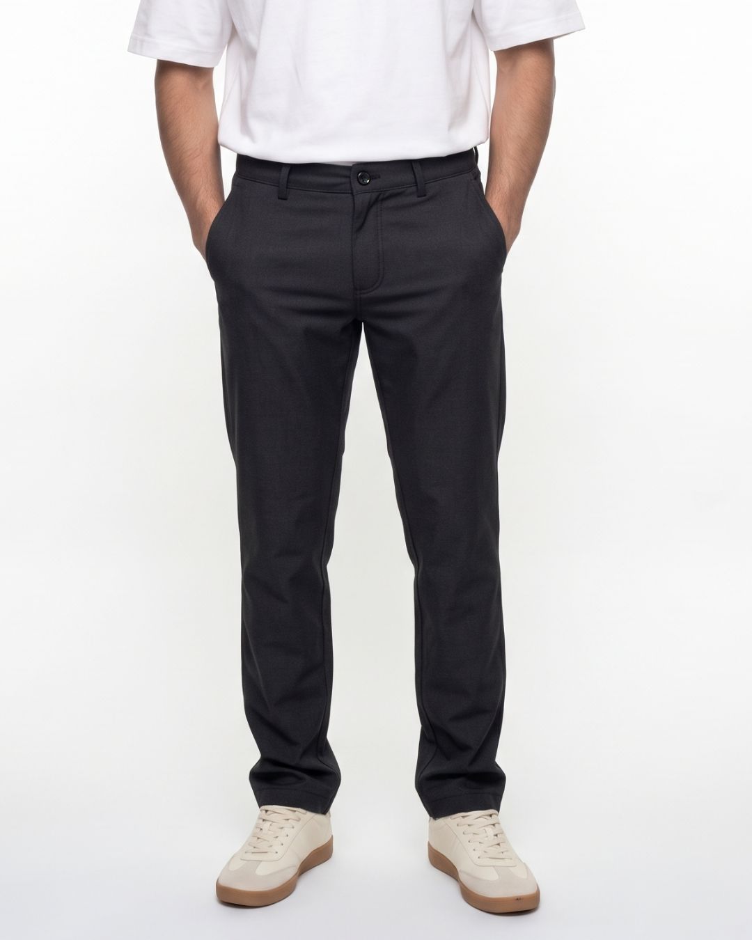 A person wearing slim-fit black trousers, paired with a white short-sleeve shirt and off-white sneakers, standing against a plain white studio background.