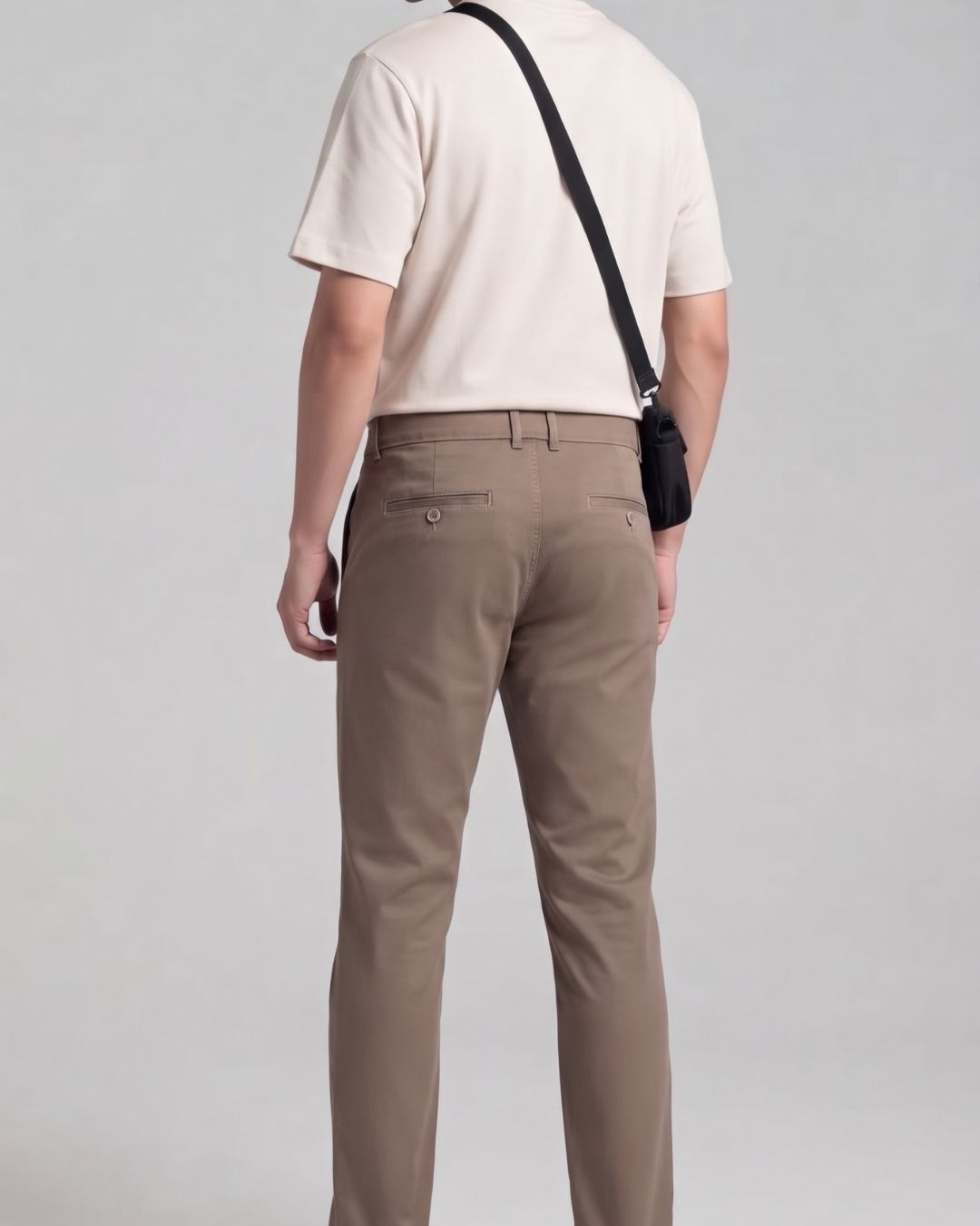A man shown from behind wearing beige trousers, a cream short-sleeve polo shirt, and carrying a small black crossbody pouch against a light gray studio background.