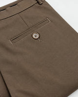 Close-up of folded brown trousers showing a rear pocket with a button closure and stitched details on a white background.