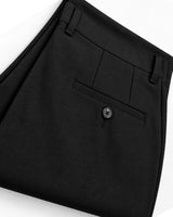 Close-up of folded black trousers showing the waistband, belt loops, front flap pocket with a button, and fabric texture on a white background.