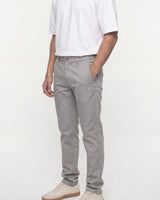 A person wearing light gray slim-fit chino pants, a white t-shirt, and beige sneakers, standing against a plain white studio background.