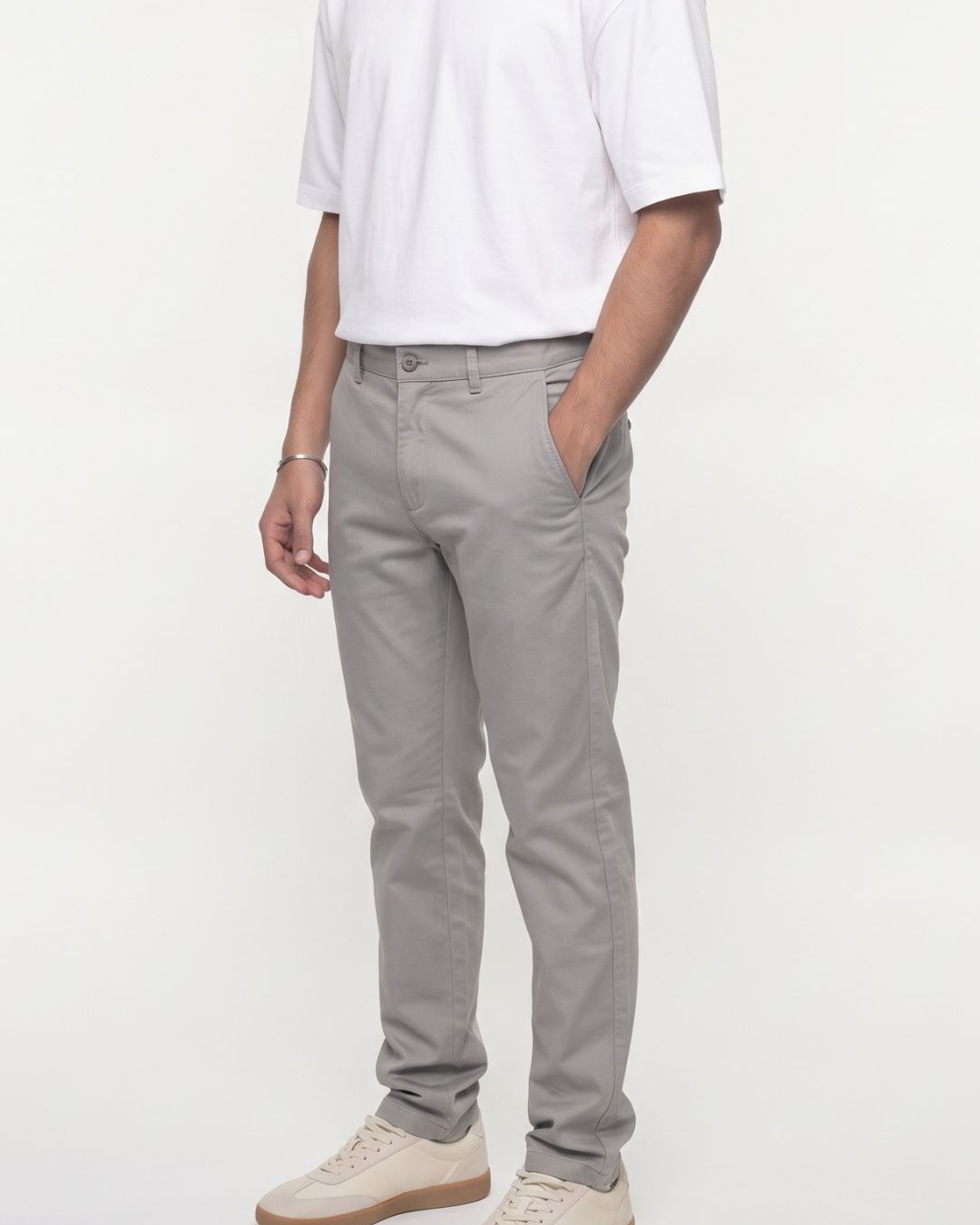 A person wearing light gray slim-fit chino pants, a white t-shirt, and beige sneakers, standing against a plain white studio background.