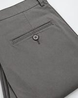 Close-up of folded gray trousers showing the back pocket with a button closure, photographed on a clean white background.