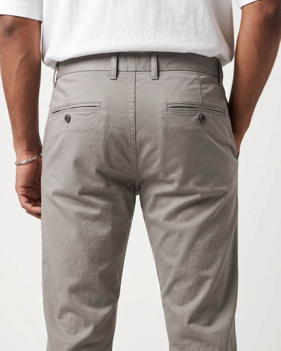 Rear view of a person wearing light gray chino pants with a white t-shirt, showing the back pockets and waistband details against a plain white background.