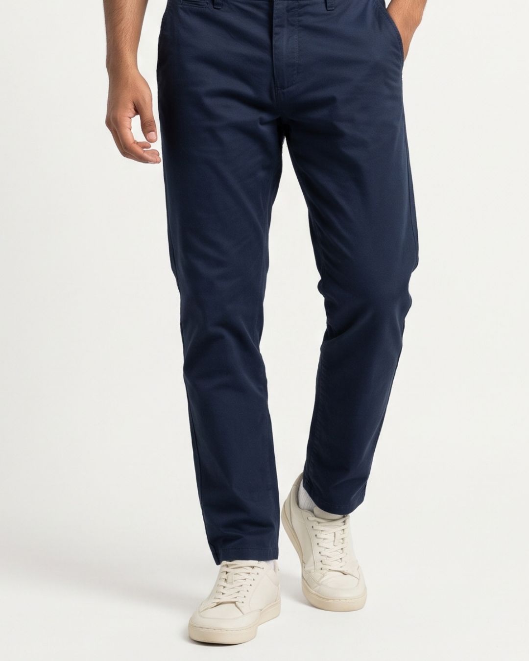 A person wearing navy blue slim-fit chinos and off-white sneakers, shown from the waist down against a clean white studio background.