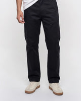A person wearing slim black pants with a white t-shirt and off-white sneakers, shown from the waist down against a plain white studio background.