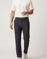 A man wearing dark charcoal gray slim-fit trousers, a cream short-sleeve t-shirt, and off-white sneakers, shown from the waist down against a light gray studio background.