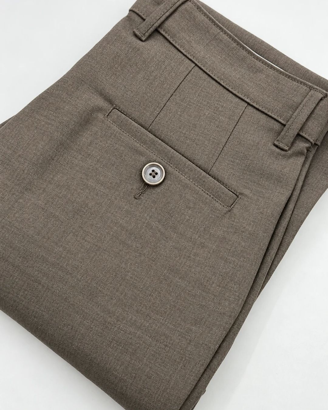 A close-up of folded brown trousers showing the waistband, belt loops, front pocket, and a single button closure on a white background.
