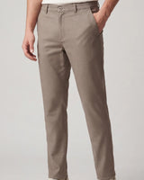 A person wearing slim-fit taupe trousers, shown from the waist down against a light gray studio background.