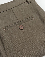 Close-up of a brown and beige micro-check patterned fabric, showing a buttoned welt pocket and belt loop detail.