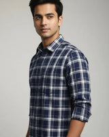 A man wearing a navy blue, white, and gray plaid long-sleeve button-down shirt, shown from the chest up against a neutral light gray background.