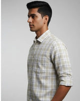 A man in profile wearing a light beige and white plaid button-down shirt with rolled-up sleeves, set against a plain light gray background.
