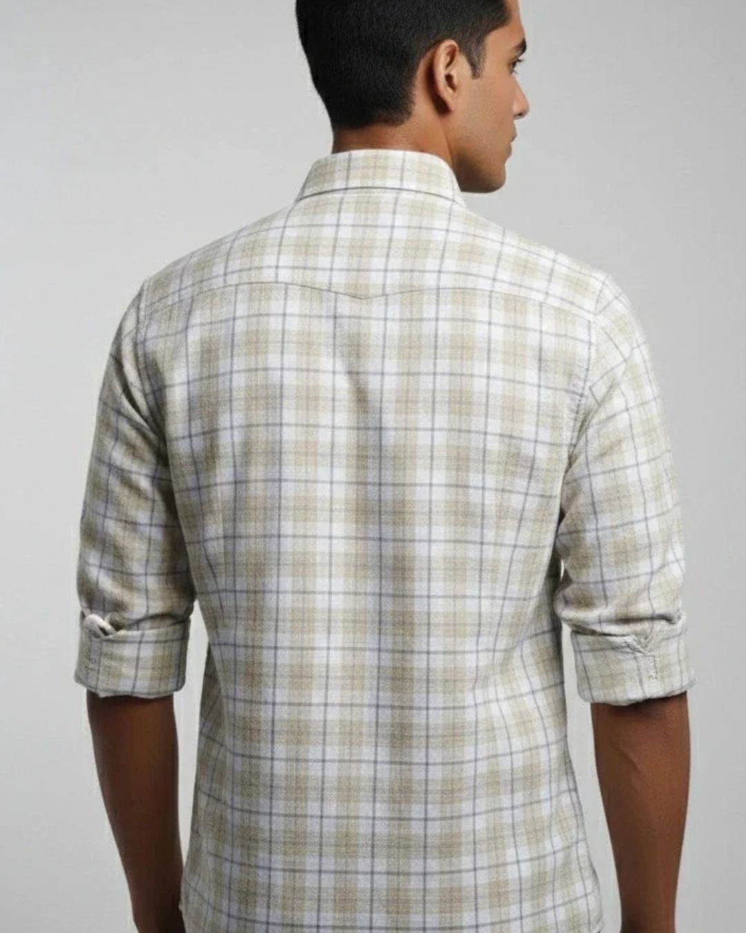 A man viewed from the back wearing a light beige and white plaid long-sleeve button-down shirt with rolled-up sleeves, set against a plain light gray background.