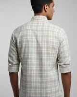 A man viewed from the back wearing a light beige and white plaid long-sleeve button-down shirt with rolled-up sleeves, set against a plain light gray background.