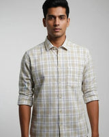 A man wearing a light beige and white plaid button-down shirt with rolled-up sleeves, photographed against a neutral gray studio background.