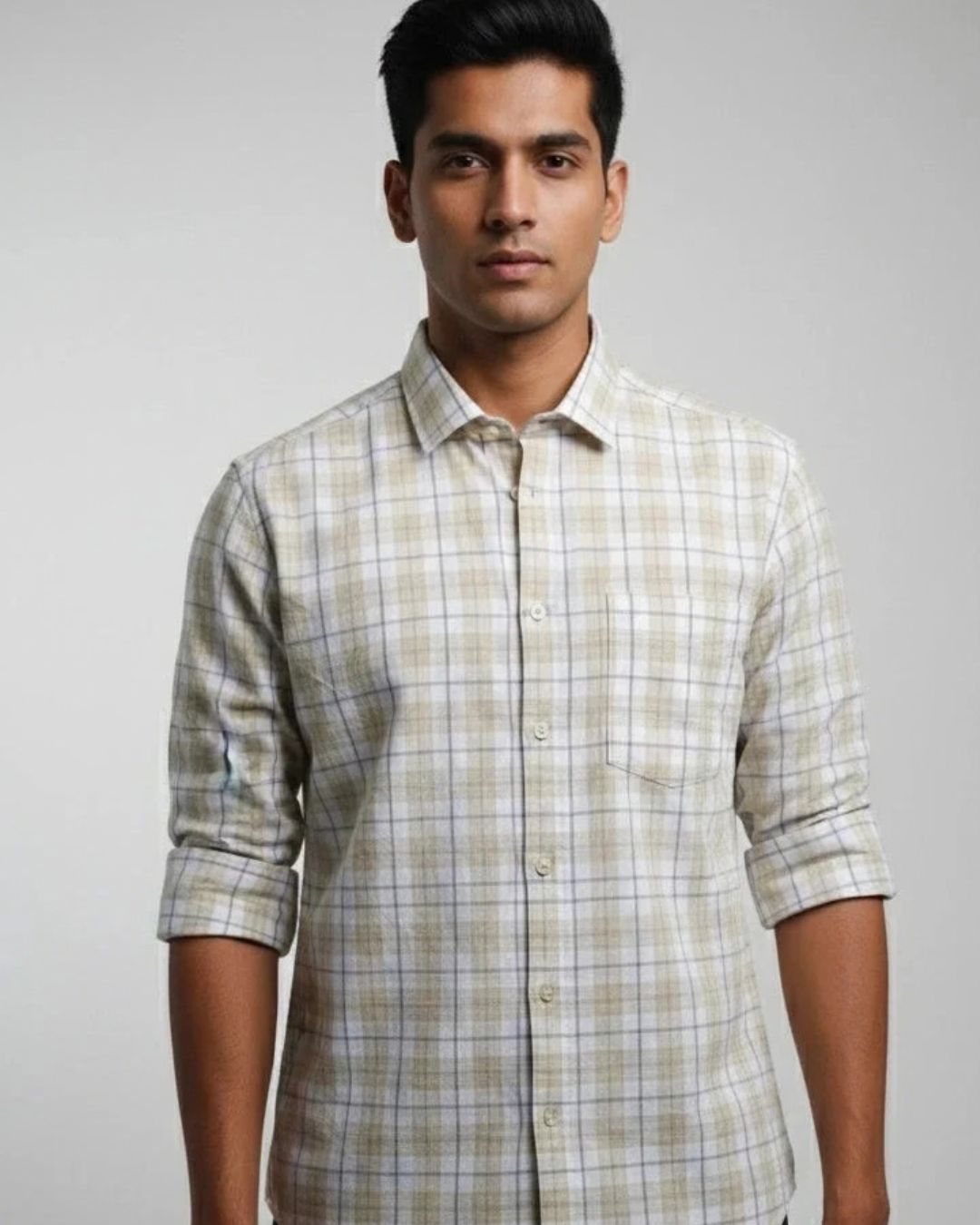A man wearing a light beige and white plaid button-down shirt with rolled-up sleeves, photographed against a neutral gray studio background.