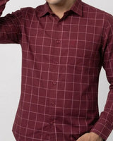 A man wearing a long-sleeve button-up shirt in maroon with a thin white windowpane grid pattern, shown against a plain light gray background.