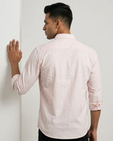A man wearing a light pink long-sleeve linen shirt, shown from the back as he stands against a white wall.