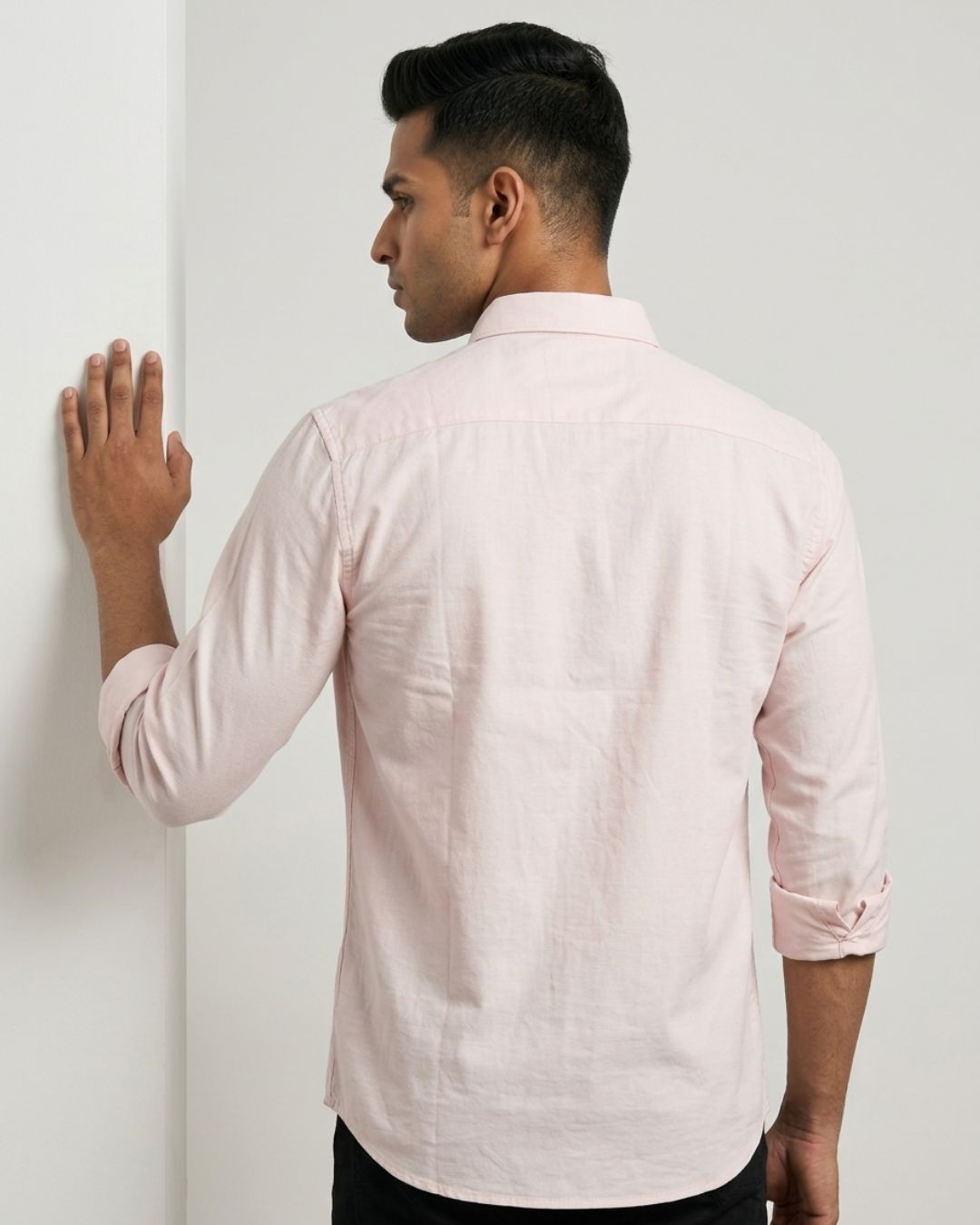 A man wearing a light pink long-sleeve linen shirt, shown from the back as he stands against a white wall.
