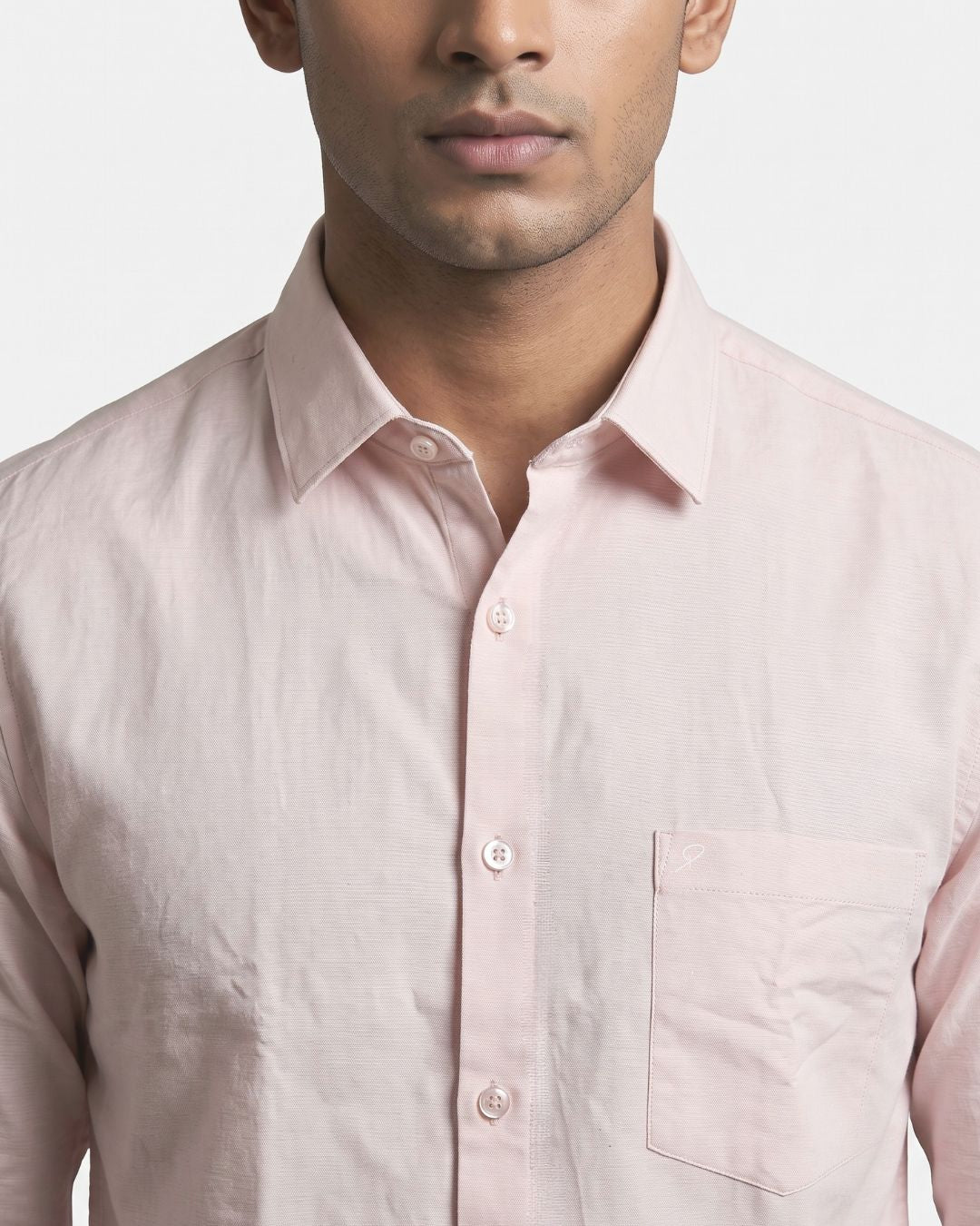 A close-up of a man wearing a light pink long-sleeve button-down shirt with a chest pocket, set against a plain light gray background.