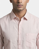 A close-up of a man wearing a light pink long-sleeve button-down shirt with a chest pocket, set against a plain light gray background.
