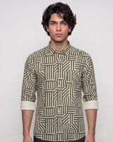 A man wearing a long-sleeve button-up shirt with a geometric striped pattern in olive green and beige, standing against a light gray background.
