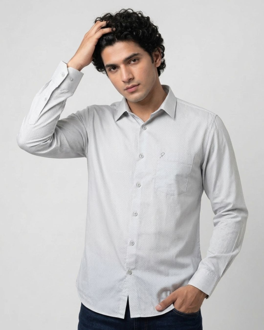 A man wearing a light gray long-sleeve button-down shirt with a chest pocket, posed against a light gray studio background.