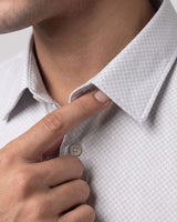 Close-up of a man wearing a light gray and white micro-patterned dress shirt, adjusting the collar with his finger.