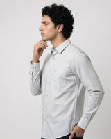 A man wearing a light gray long-sleeve button-down shirt, shown in a side profile against a plain light gray studio background.