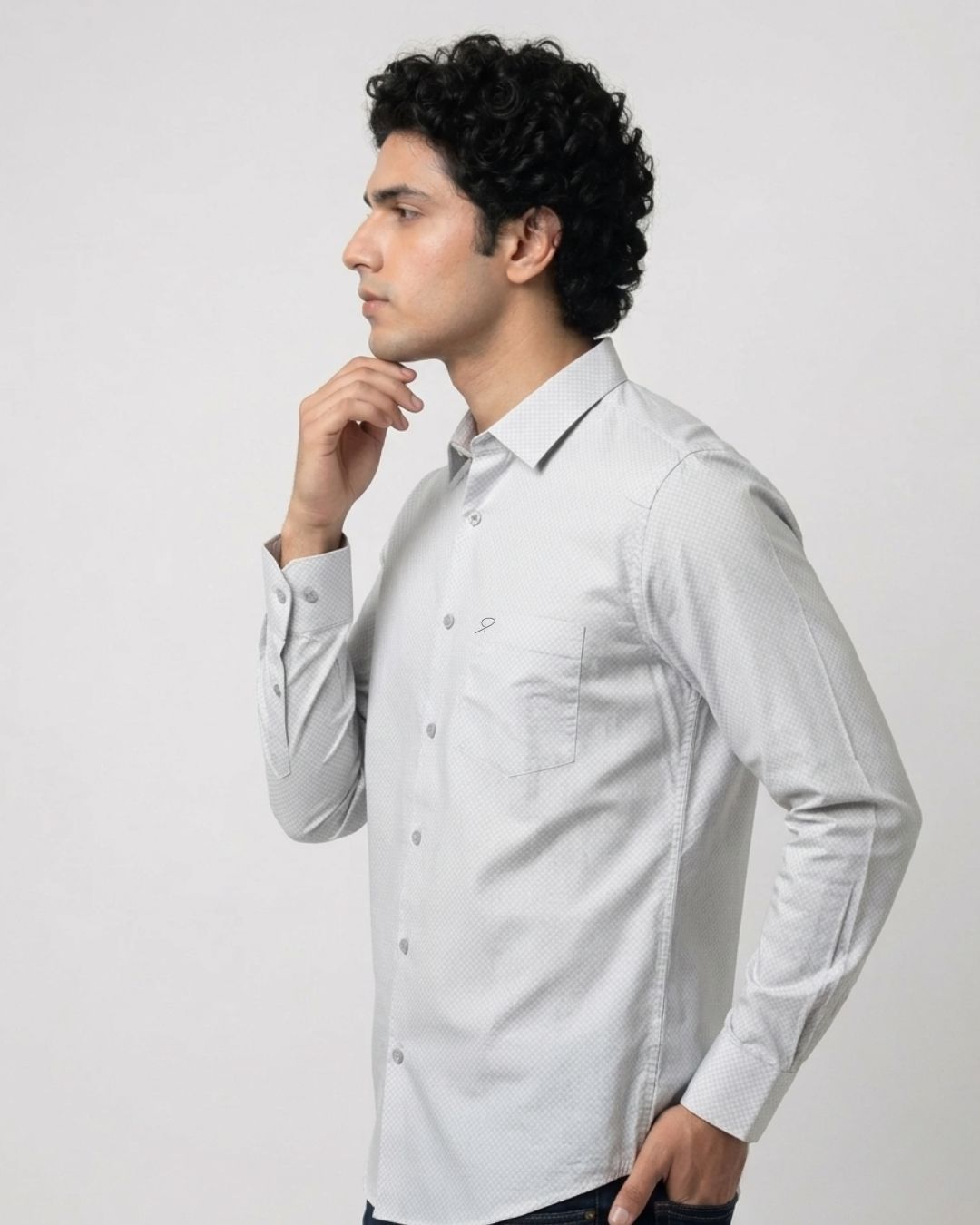 A man wearing a light gray long-sleeve button-down shirt, shown in a side profile against a plain light gray studio background.