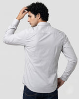 A man wearing a light gray long-sleeve button-down shirt, shown from the back, paired with dark blue jeans against a plain light gray studio background.