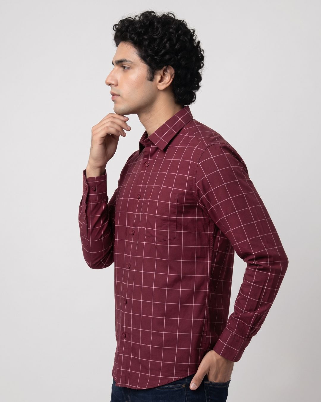 A man wearing a long-sleeve burgundy button-up shirt with a white windowpane grid pattern, shown in profile against a light gray studio background.