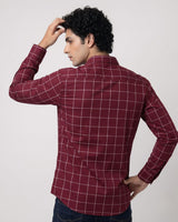 A man wearing a burgundy long-sleeve button-down shirt with a white windowpane grid pattern, shown from the back against a light gray studio background.