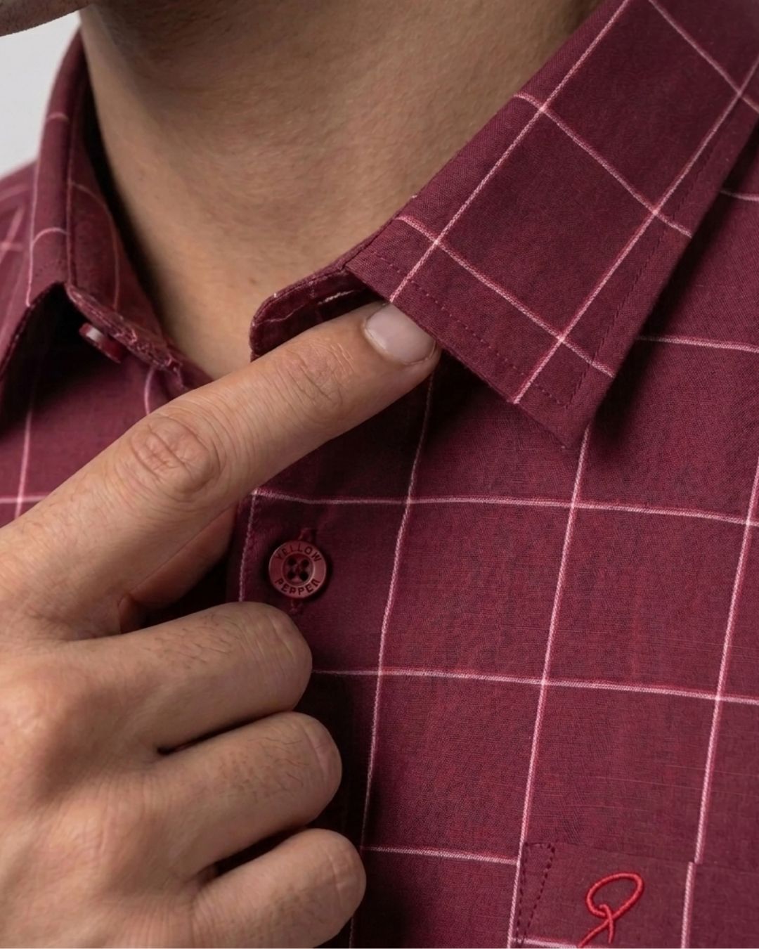 Close-up of a person wearing a burgundy plaid button-down shirt, pointing to the collar and button area.